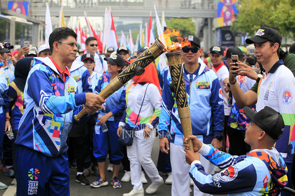 Wakil Ketua KPK Laode M Syarief (kiri) menyalakan api obor yang dibawa atlet bola basket kursi roda Indonesia pada Asian Para games 2018, Derry ketika acara pawai obor api APG 2018 saat melintas di Jalan MH Thamrin, Jakarta.