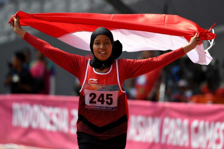 Sprinter Indonesia Karisma Evi Tiarani melakukan selebrasi dengan mengibarkan bendera Merah Putih usai finis terdepan dalam nomor 100 meter putri T42 dan T63 Asian Para Games 2018 di Stadion Utama Gelora Bung Karno, Jakarta, Rabu, 10 Oktober.