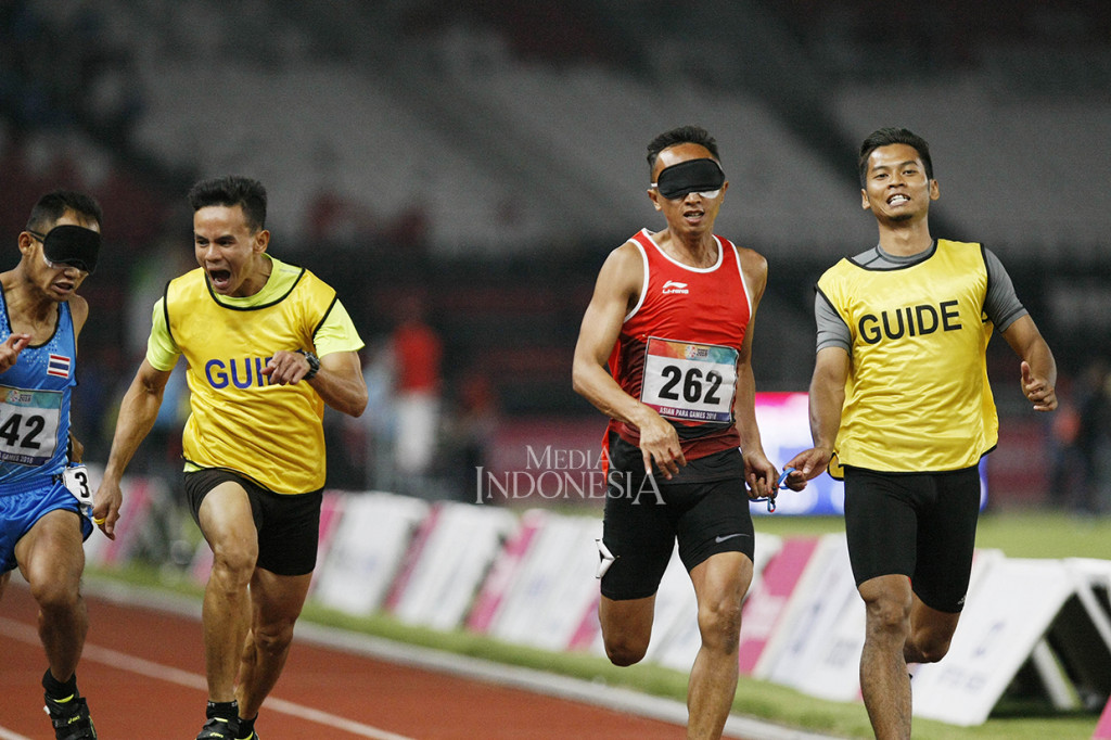 Sprinter Indonesia Abdul Halim Dalimunthe (262) bersama pendampingnya memacu kecepatan saat mengikuti final lari 100 meter putra T11 Asian Para Games 2018 di Stadion Utaama GBK, Senayan, Jakarta.