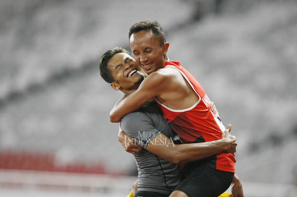 Sprinter Indonesia Abdul Halim Dalimunthe (262) melakukan selebrasi bersama pendampingnya seusai finis kedua pada final lari 100 meter putra T11 Asian Para Games 2018 di Stadion Utaama GBK, Senayan, Jakarta.