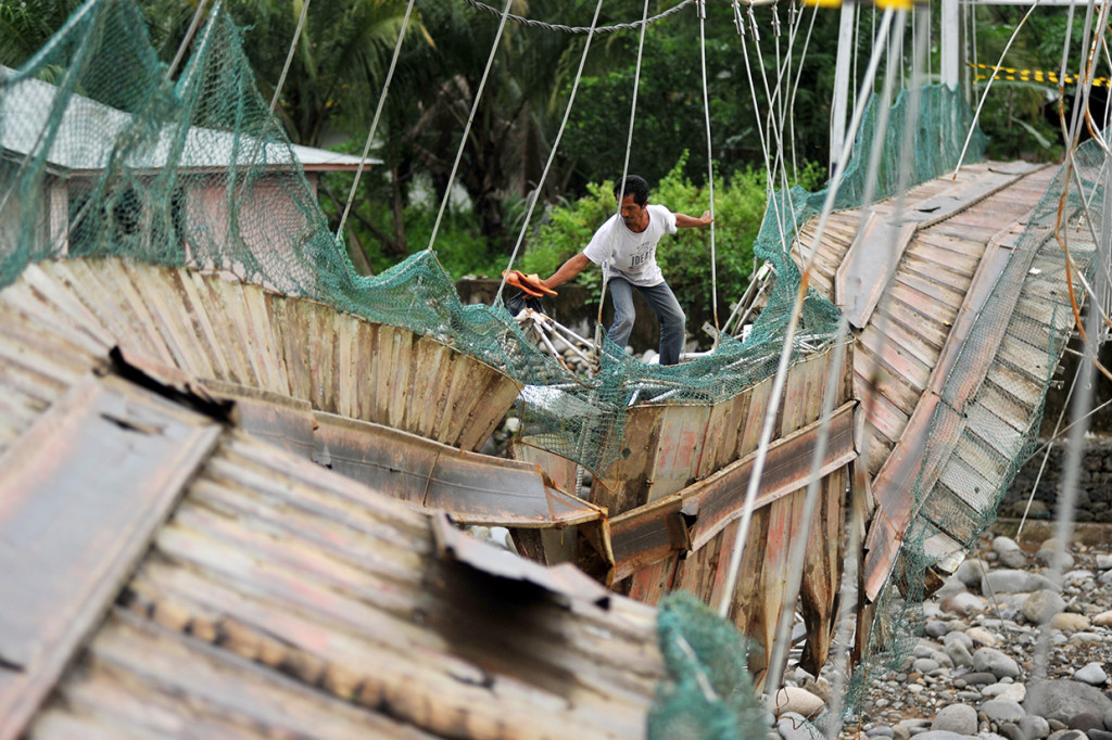 Warga melewati jembatan yang rusak di Kelurahan Baringin, Lubuk Kilangan, Padang, Sumatera Barat.