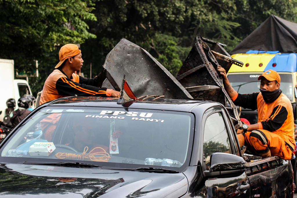 Petugas kebersihan mengangkut barang sisa perusakan dan pembakaran di Polsek Ciracas, Jakarta.