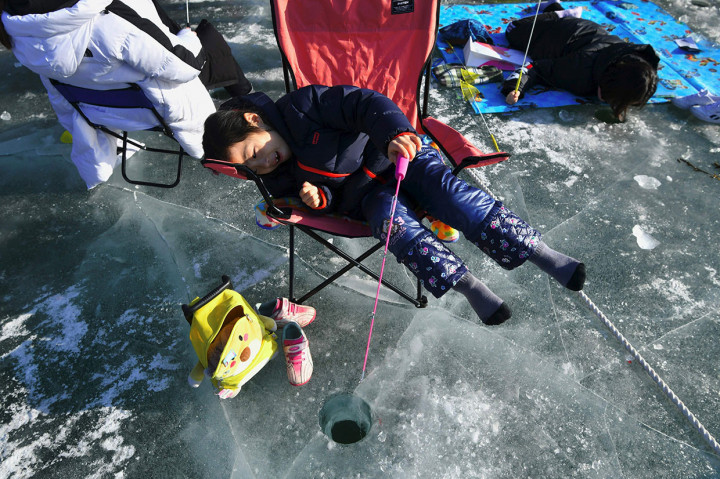 Seorang anak memancing ikan di sungai beku Hwacheon sambil bersandar di kursi, sementara pengunjung lainnya sambil tiduran. 