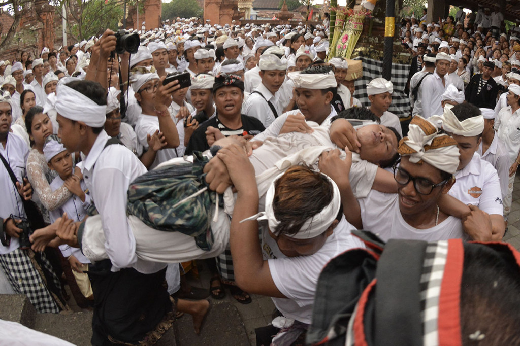 Sejumlah umat Hindu menenangkan seorang umat yang kesurupan saat Tradisi Ngerebong di Pura Dalem Pengrebongan, Denpasar, Bali.