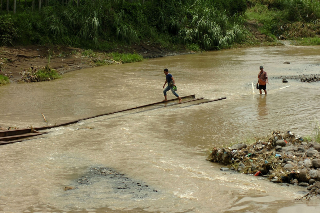Dua warga menyeberangai Sungai Kemisik samping jembatan yang ambruk di Desa Wanasari, Kabupaten Tegal, Jawa Tengah.