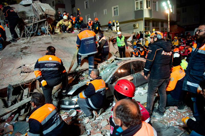 Sebuah mobil rusak parah tertimpa reruntuhan apartemen.