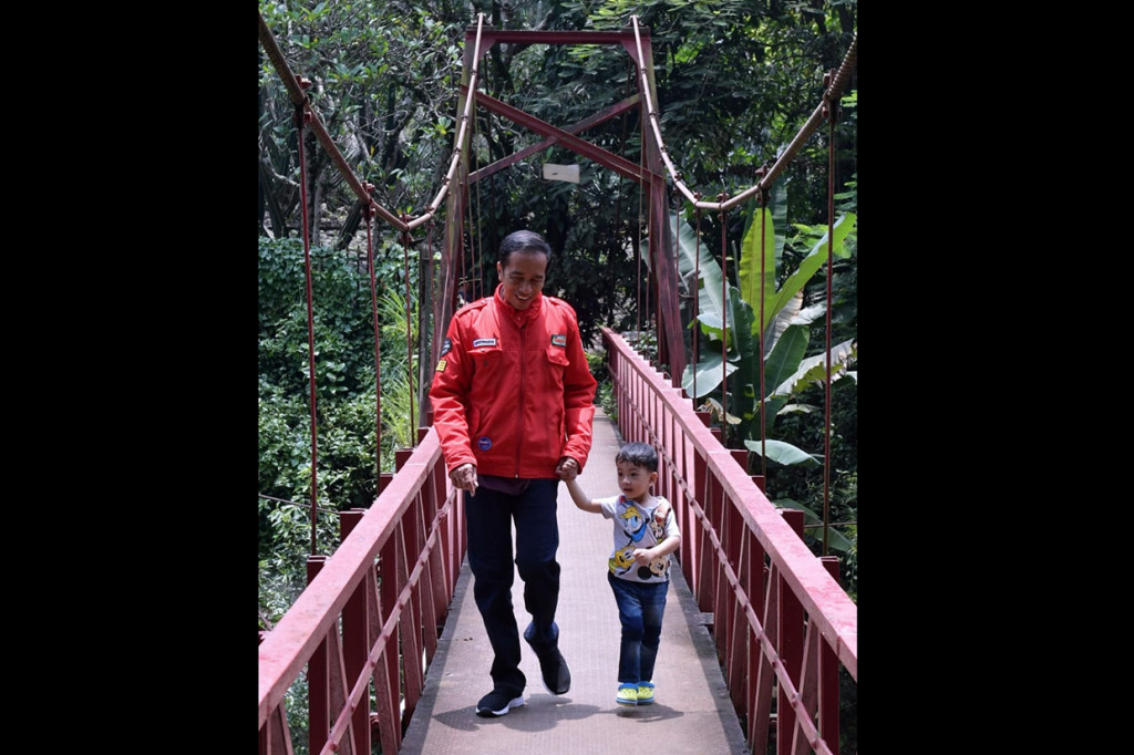 Jokowi mengenakan jaket merah menggandeng Jan Ethes yang memakai kaus berwarna putih dan celana jin biru. Putra Gibran Rakabuming Raka dan Selvi Ananda itu tampak senang saat kakenya mengajak jalan-jalan di Kebun Raya Bogor.