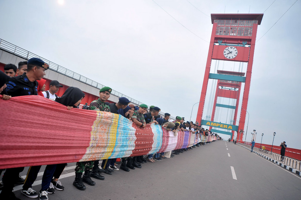Kain warna-warni khas Kota Pempek sepanjang 1,177 Km itu dibentangkan oleh anggota TNI, Polri, mahasiswa, dan masyarakat umum dari pangkal hingga ujung Jembatan Ampera.