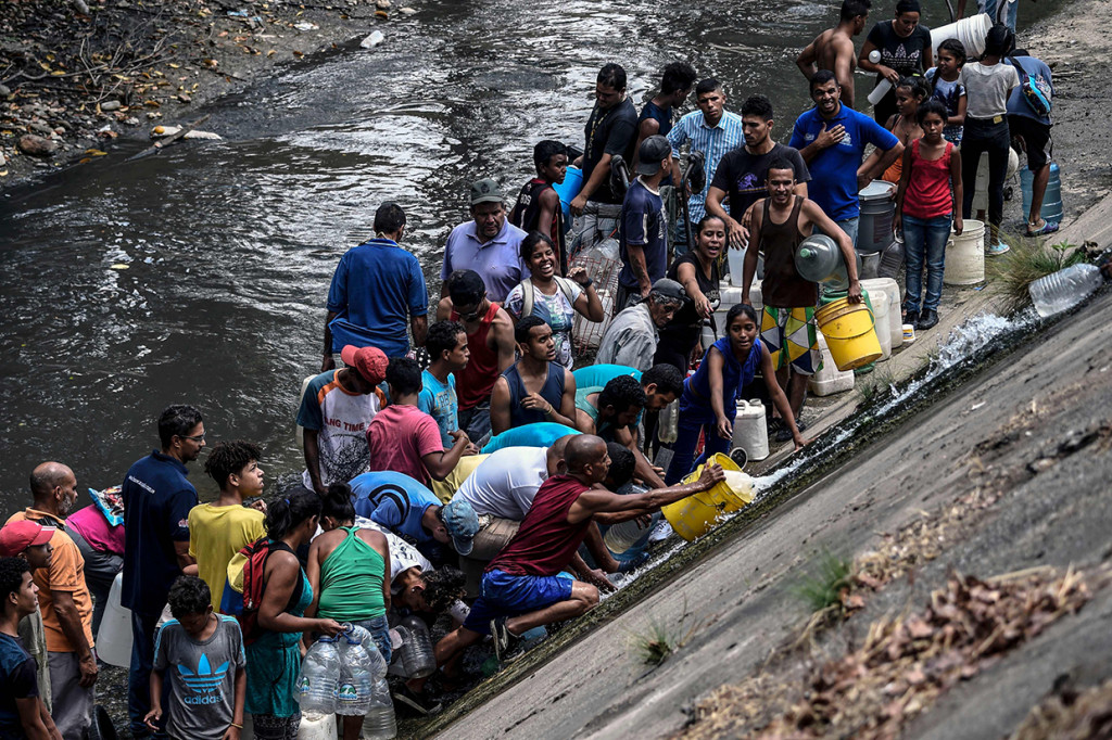 Warga mengumpulkan air yang keluar dari saluran pembuangan limbah ke Sungai Guaire di Caracas, Venezuela. Afp Photo/Juan Barreto