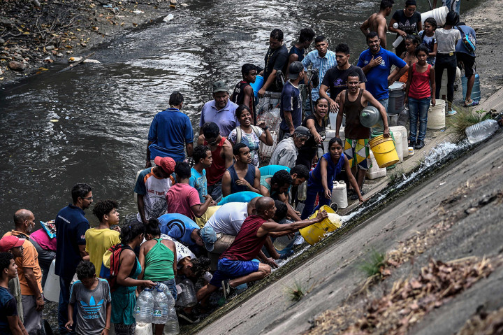 Warga mengumpulkan air yang keluar dari saluran pembuangan limbah ke Sungai Guaire di Caracas, Venezuela. Afp Photo/Juan Barreto
