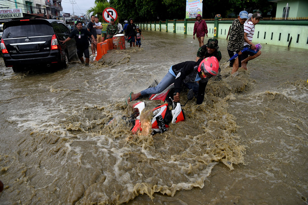 Seorang pengendara terjatuh ketika berusaha menerobos banjir di Sentani, Jayapura, Papua.