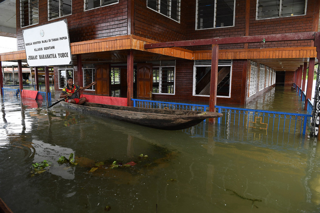 Warga menggunakan perahu melintas di depan gereja yang terendam banjir akibat meluapnya Danau Sentani dampak dari banjir bandang Sentani di Kampung Yoboi, Danau Sentani.Antara Foto/Zabur Karuru
