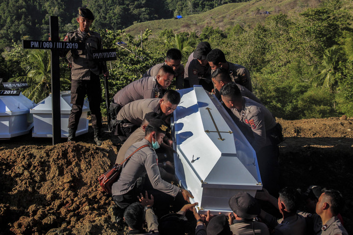 Personil kepolisian memasukkan peti berisi jenazah korban banjir bandang Sentani yang dikuburkan secara massal di Pemakaman Umum Kampung Harapan Sentani, Jayapura, Papua.