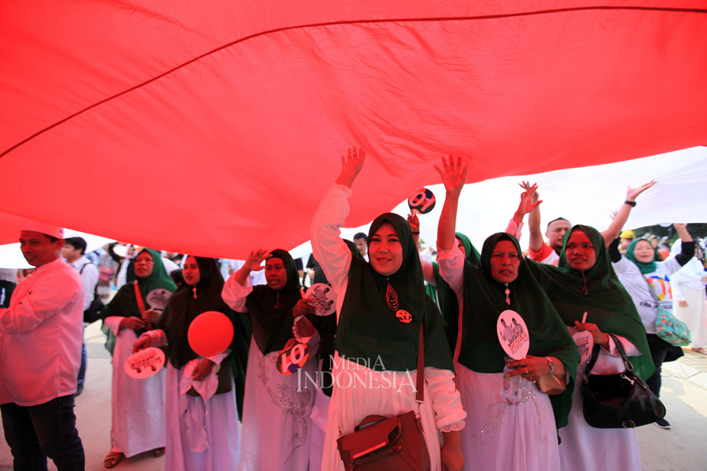 Sejumlah simpatisan mengibarkan bendera merah putih raksasa ketika menyaksikan calon Wakil Presiden nomor urut 01 KH Ma'ruf Amin bersama sejumlah pendukung acara menyanyikan lagu Indonesia Raya ketika berkampanye di Parkir Timur Komplek GBK, Senayan, Jakarta.