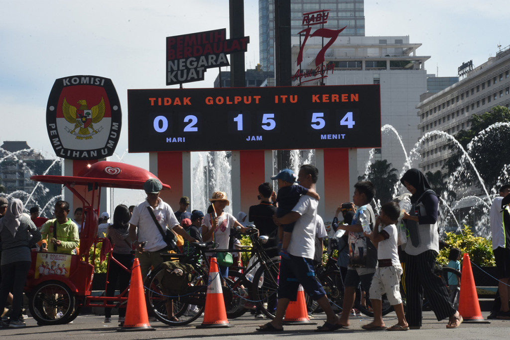 Warga melintas di depan monitor hitung mundur pelaksanaan Pemilu sebagai bagian dari sosialisasi di Bundaran HI, Jakarta.