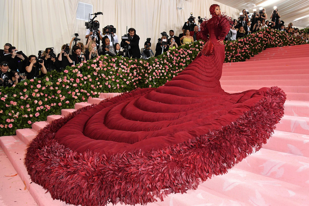 Bak burung raksasa berjalan, Cardi B menyapu karpet merah dengan gaun panjang dan lebar berwarna merah lengkap dengan detail bulu berwarna serupa. Tampilan juga dilengkapi oleh headpiece berhiaskan berlian merah dan sarung tangan warna senada.