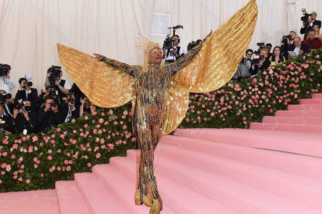 Billy Porter membuat karpet merah Met Gala 2019 hening. Dia tampil bak Dewa Matahari dengan catsuit berhias berlian dilengkapi sayap dan headpiece emas 24 karat karya The Blonds.