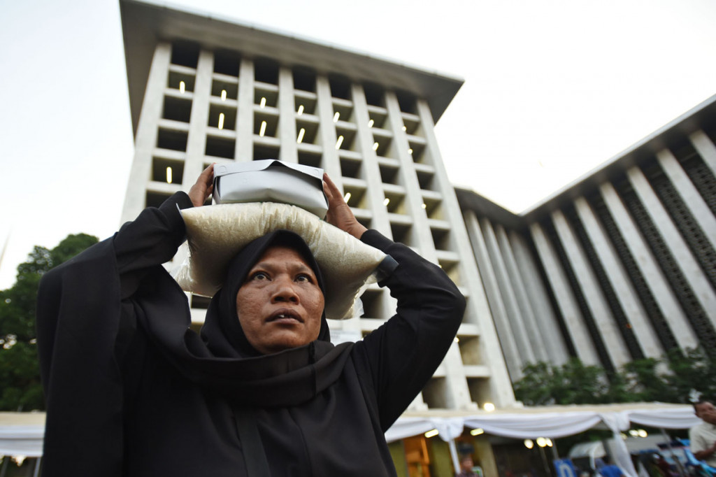 Seorang mustahik (warga penerima zakat) menyunggi beras zakat fitrah yang dia terima di Masjid Istiqlal, Jakarta. 