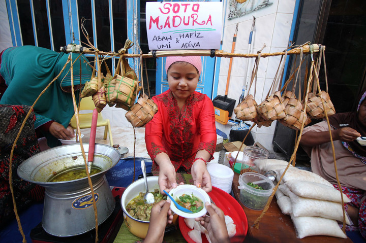 Seorang anak melayani warga yang ingin menikmati hidangan ketupat gratis di Kampung Sukolilo, Kenjeran, Surabaya, Jawa Timur, Rabu, 12 Juni 2019. Tradisi Lebaran Ketupat yang dirayakan pada hari ketujuh setelah Idul Fitri di kampung tersebut dimeriahkan dengan membagikan hidangan ketupat secara gratis, sebagai ungkapan rasa syukur dan mempererat persaudaraan. Antara Foto/Moch Asim