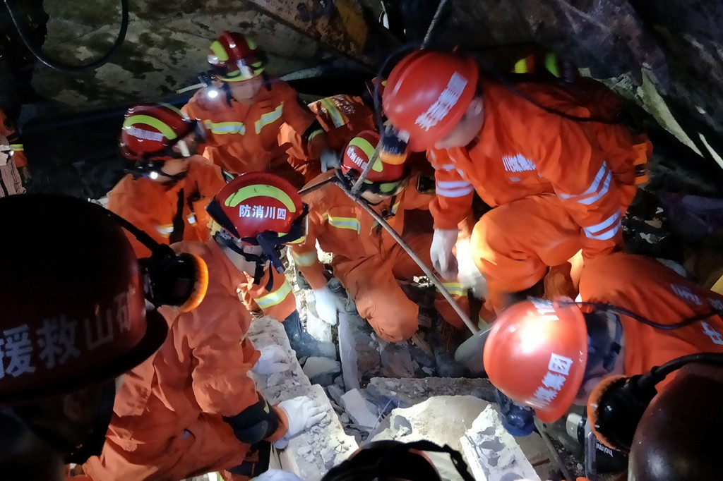 Para petugas penyelamat berusaha mengeluarkan seorang penyintas dari balik reruntuhan bangunan.