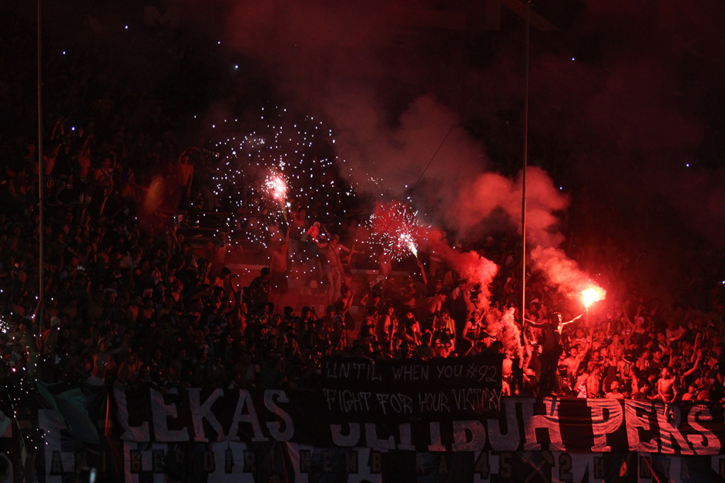 Suporter Persebaya menyalakan suar dan kembang api saat pertandingan babak delapan besar Piala Indonesia melawan Madura United di Stadion Gelora Bung Tomo.