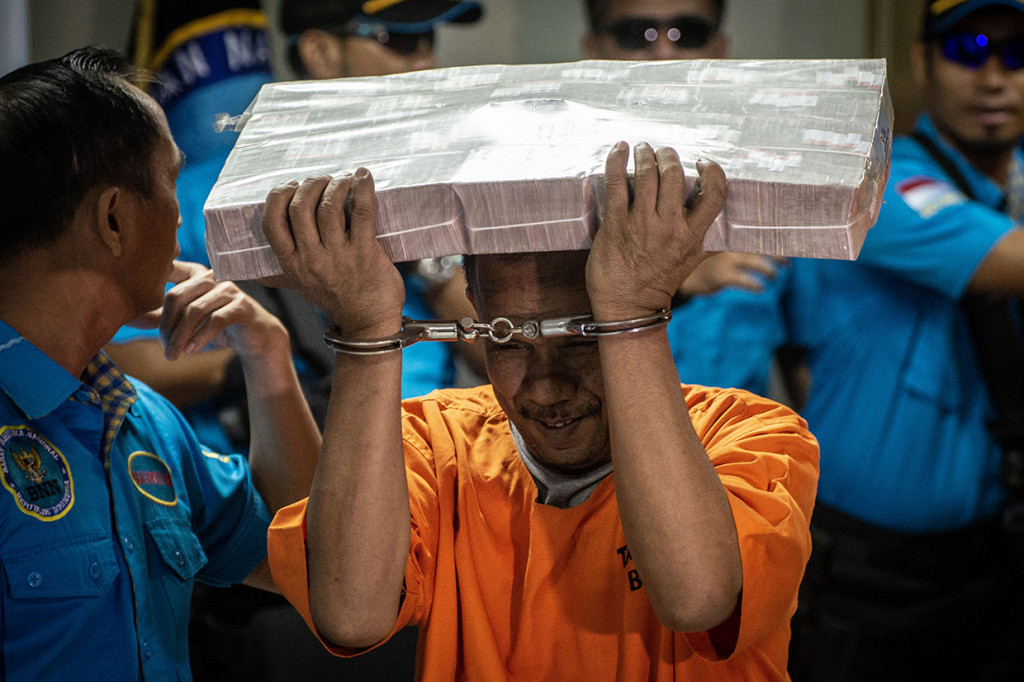 Seorang tersangka membawa di atas kepala barang bukti berupa uang tunai yang dihadirkan dalam rilis kasus Tindak Pidana Pencucian Uang (TPPU) dari tindak kejahatan narkotika, di Kantor Badan Narkotika Nasional (BNN), Jakarta.