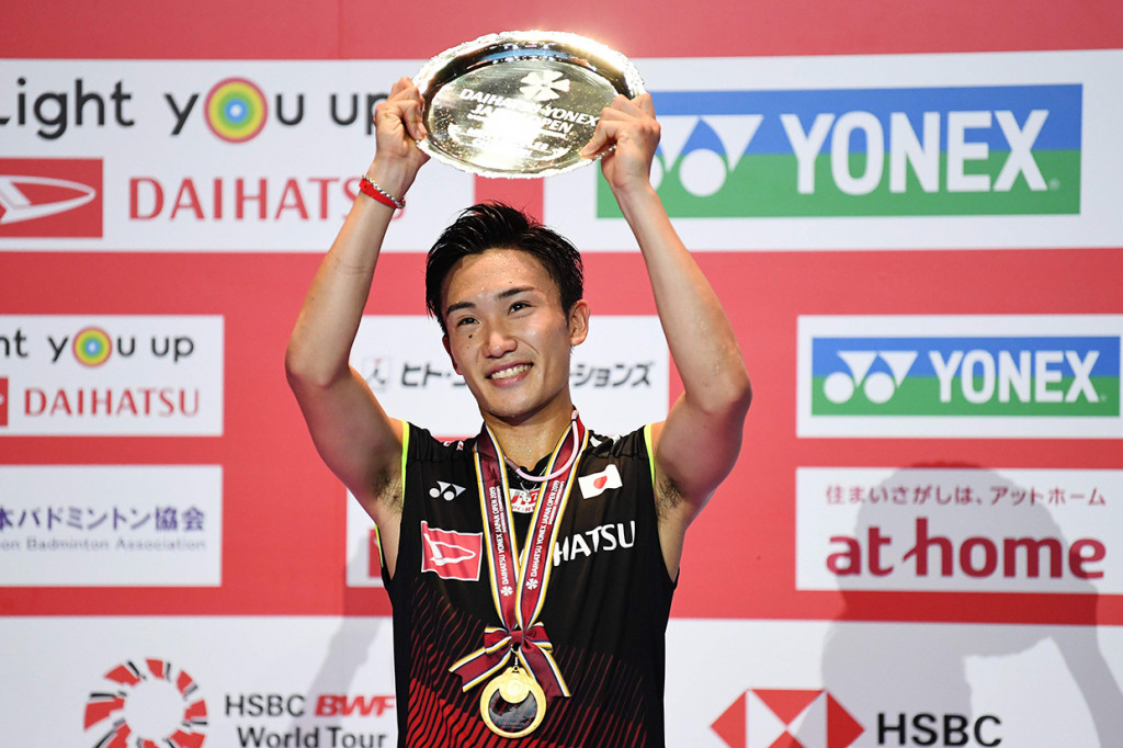 Pebulutangkis Jepang Kento Momota mengangkat trofi setelah menjadi juara Japan Open 2019.