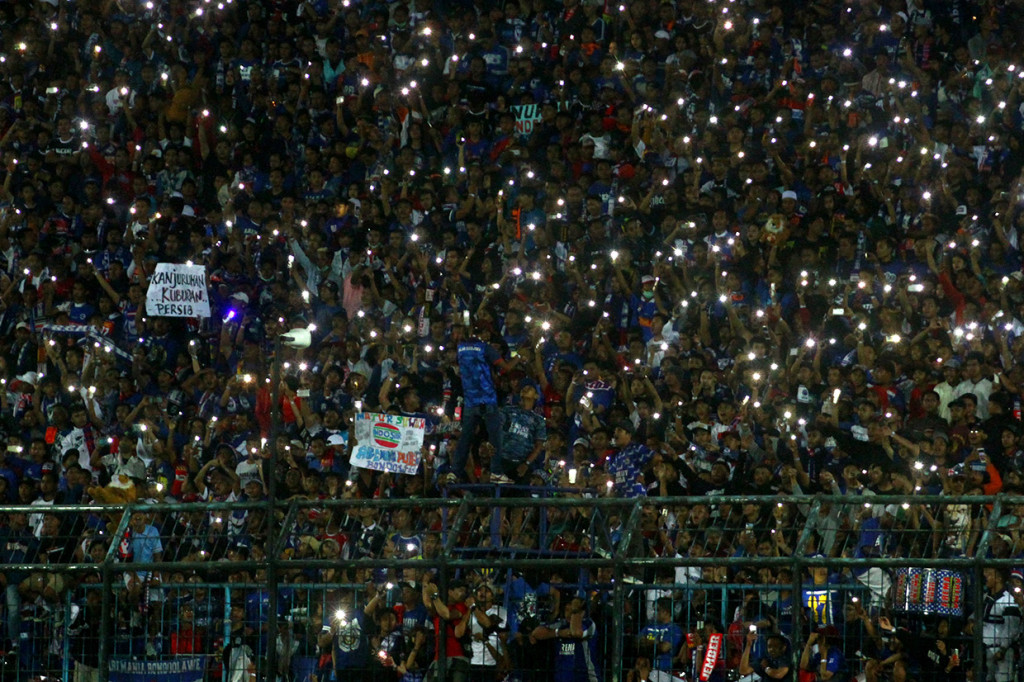 Suporter Arema FC (Aremania) beratraksi dengan menyalakan lampu gawai usai pertandingan Liga I antara Arema melawan Persib Bandung di stadion Kanjuruhan, Malang, Jawa Timu. 