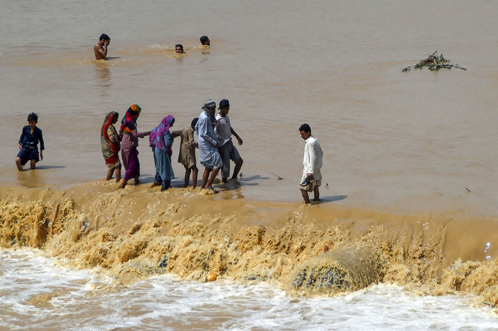 Warga dengan penuh hati-hati melewati genangan banjir untuk mengungsi ke tempat yang lebih aman di Karachi.