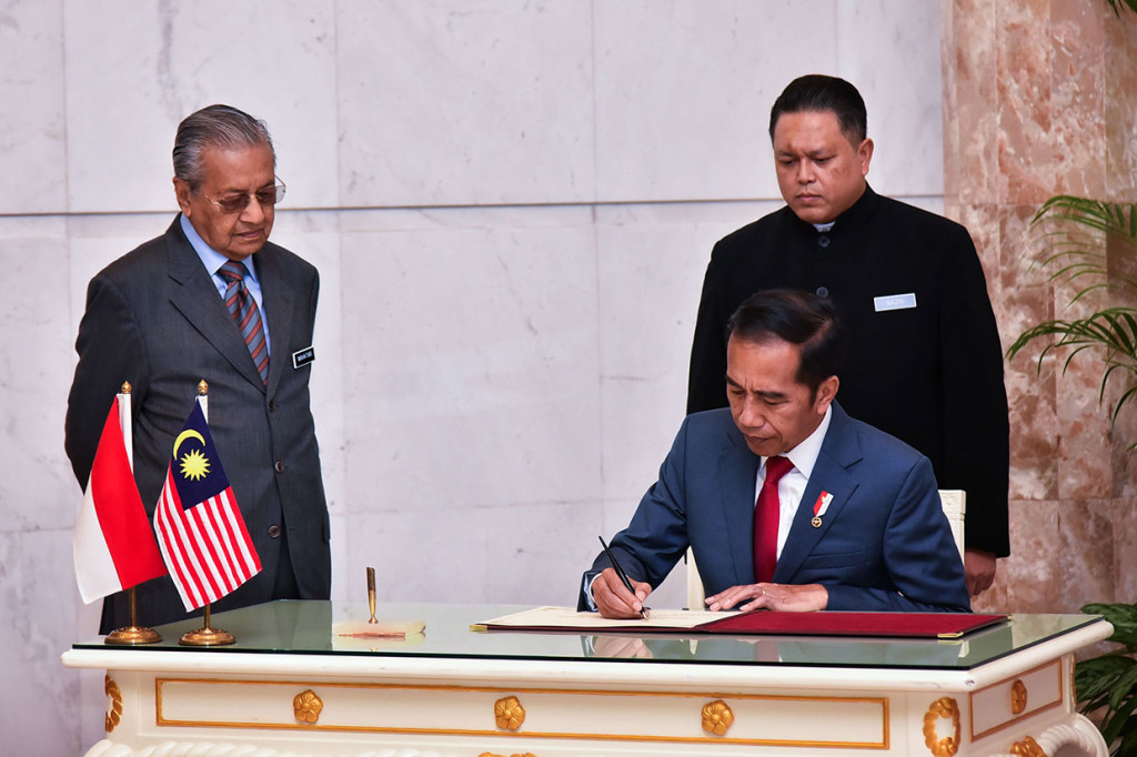 Jokowi mengisi buku tamu disaksikan Mahathir Mohamad.