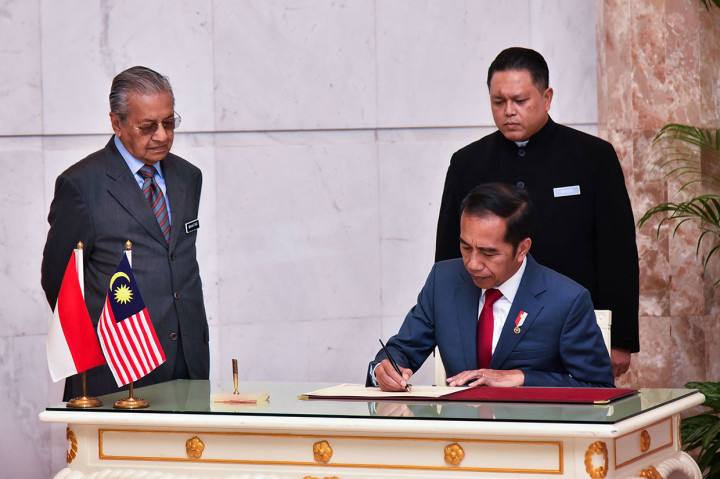 Jokowi mengisi buku tamu disaksikan Mahathir Mohamad.