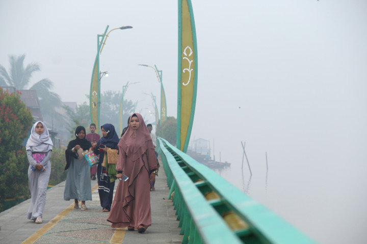 Umat Muslim yang akan menunaikan ibadah Salat Idul Adha berjalan di tepian Sungai Kapuas yang diselimuti kabut asap di Pontianak, Kalimantan Barat. Antara Foto/Jessica Helena Wuysang
