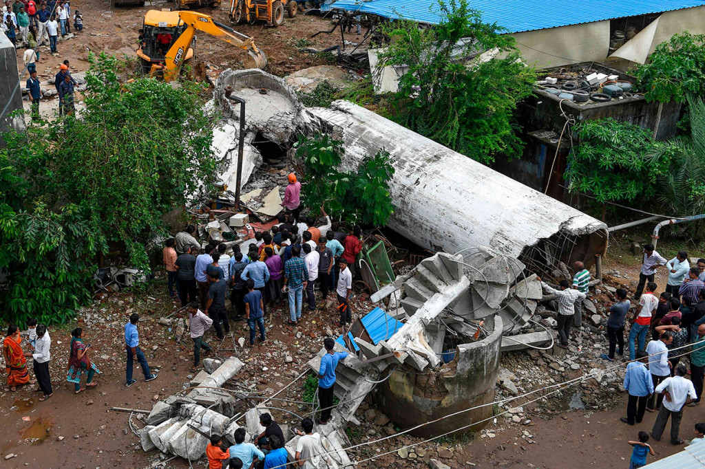 Warga berkerumun saat petugas penyelamat mencari korban di antara reruntuhan tangki air yang runtuh di daerah Bopal, Ahmedabad, India, Senin, 12 Agustus 2019.