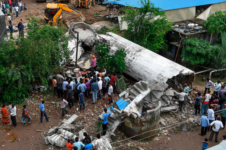 Warga berkerumun saat petugas penyelamat mencari korban di antara reruntuhan tangki air yang runtuh di daerah Bopal, Ahmedabad, India, Senin, 12 Agustus 2019.