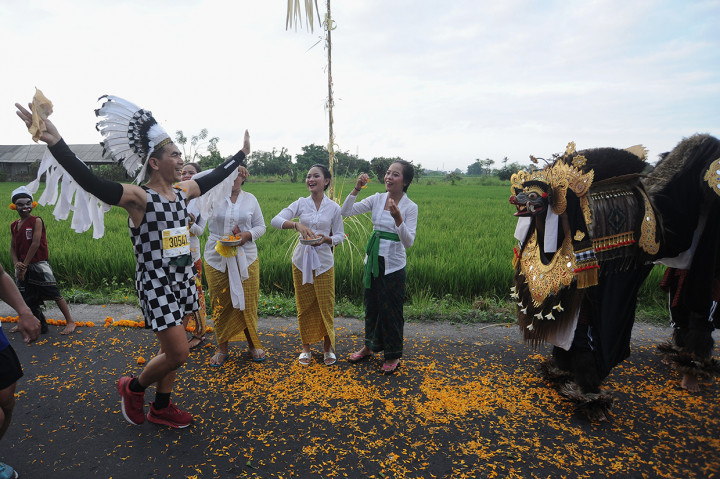 Seorang peserta berlari di dekat penari Barong saat mengikuti Maybank Bali Marathon 2019 di kawasan Klungkung, Bali.