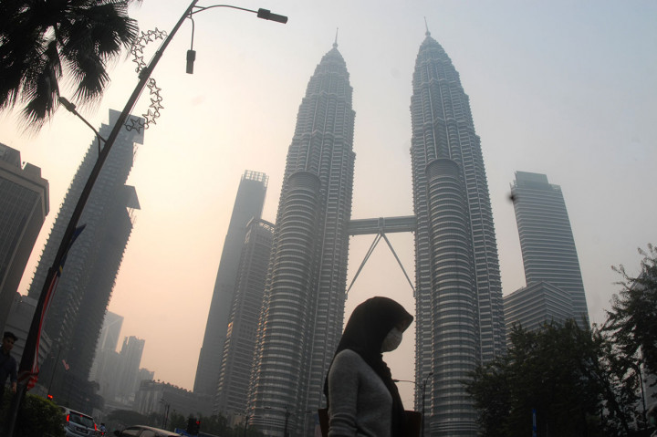 Warga beraktivitas dengan mengenakan masker dengan latar belakang menara kembar Petronas, Kuala Lumpur, Malaysia, yang diselimuti kabut asap, Selasa, 10 September 2019. Antara Foto/Rafiuddin Abdul Rahman