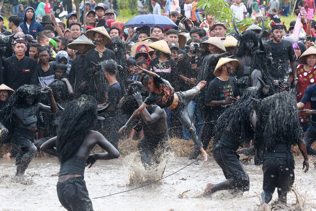 Warga yang berdandan kebo-keboan (kerbau) menceburkan penonton ke dalam kubangan pada ritual adat Kebo-keboan Alasmalang, Banyuwangi, Jawa Timur.