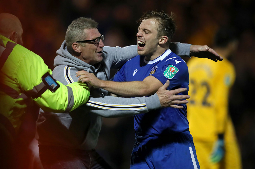 Tom Lapslie meluapkan kegembiraan bersama ofisial tim usai menjadi penentu kemenangan timnya lewat drama adu penalti. Colchester United melaju ke babak 16 besar Piala Liga Inggris dengan kemenangan 4-3.