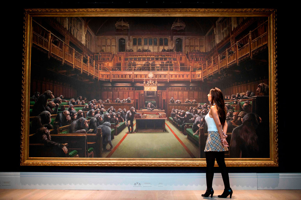 Seorang asisten galeri berpose di depan lukisna berjudul 'Devolved Parliament' karya seniman Inggris Banksy, dalam sebuah konferensi pers di London pada 27 September 2019. Lukisan tersebut akan dilelang pekan depan dengan perkiraan nilai jual lebih dari Rp35,4 miliar.