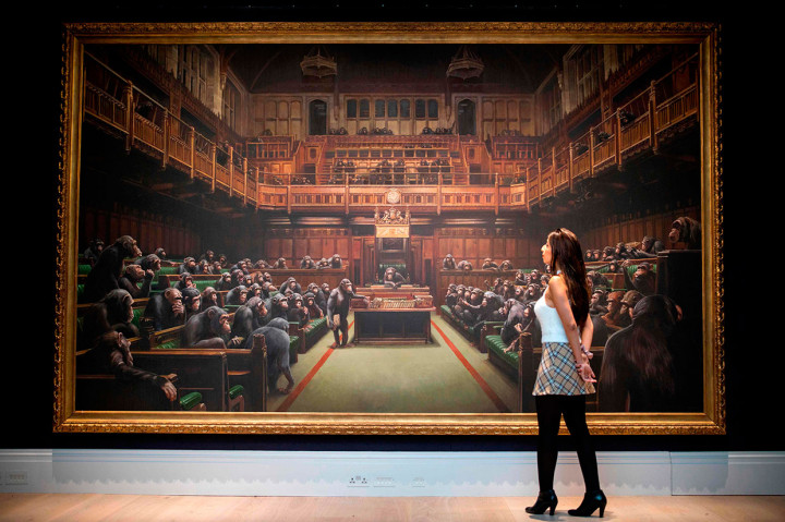 Seorang asisten galeri berpose di depan lukisna berjudul 'Devolved Parliament' karya seniman Inggris Banksy, dalam sebuah konferensi pers di London pada 27 September 2019. Lukisan tersebut akan dilelang pekan depan dengan perkiraan nilai jual lebih dari Rp35,4 miliar.