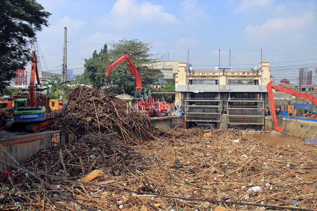 Pekerja UPK Badan Air Dinas Lingkungan Hidup DKI Jakarta menggunakan alat berat membersihkan sampah yang menumpuk di Pintu Air Manggarai, Jalan Tambak, Kecamatan Menteng, Jakarta Pusat, Rabu, 9 Oktober 2019.