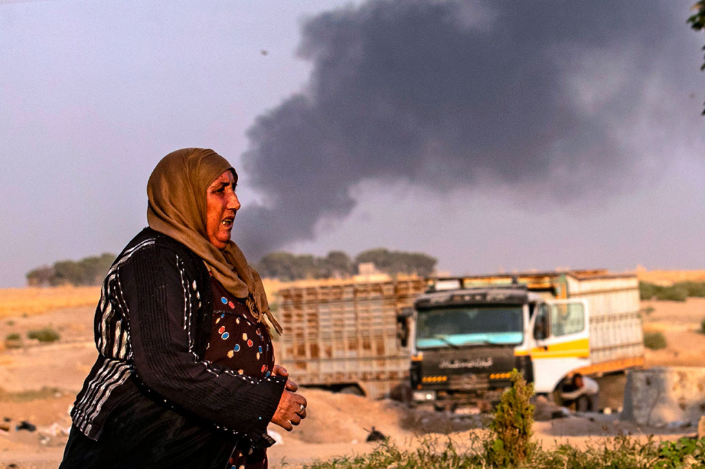 Seorang perempuan dengan muka cemas berlari untuk mencari tempat berlindung akibat serangan yang dilancarkan Turki di wilayah yang dikuasai Kurdi di Kota Ras al-Ain, Provinsi Hasakeh, wilayah timur laut Suriah.