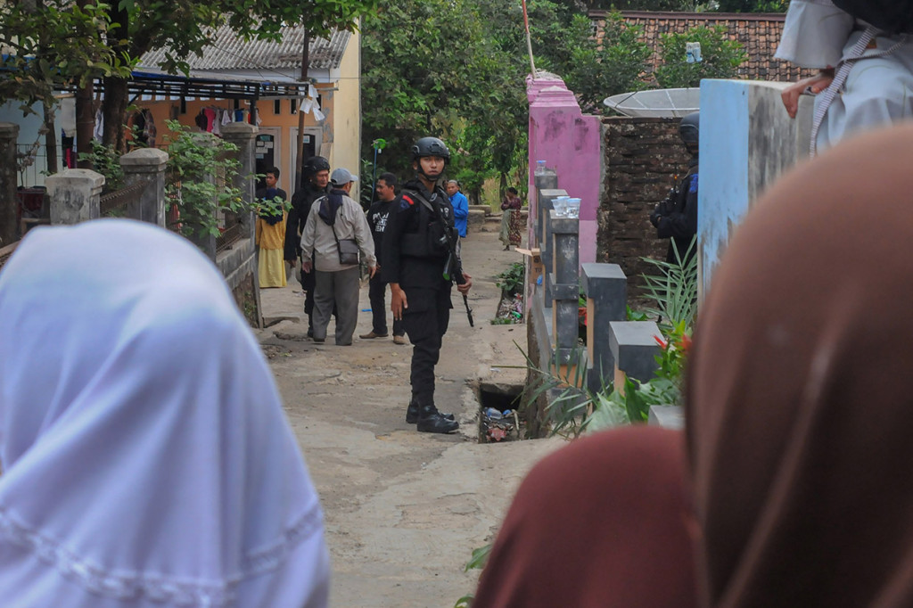 Polisi bersenjata lengkap berjaga di depan rumah kontrakan Syahril tersangka penusukan Menkopolhukam Wiranto di Kampung Sawah, Desa Menes, Pandeglang, Banten. Kontrakan tersebut telah dipasangi garis polisi.