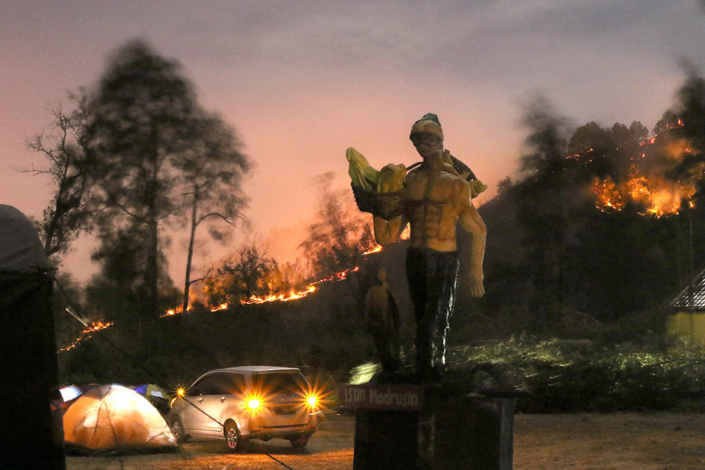 Wisatawan mendirikan tenda di Pos Pendakian Gunung Ijen saat Gunung Widodaren terbakar terlihat dari Paltuding, Banyuwangi, Jawa Timur.