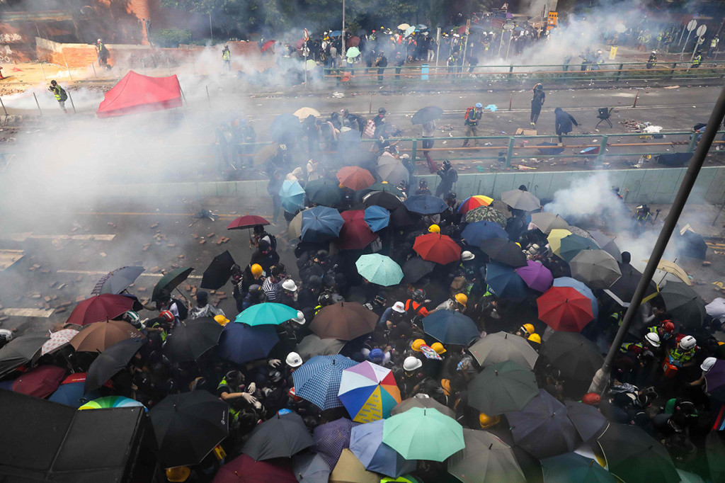 Para pengunjuk rasa berjongkok di bawah payung untuk menghindari meriam air polisi yang sesekali ditembakan ke arah mereka. Beberapa pedemo bahkan turut melemparkan bom molotov ke sebuah kendaraan lapis baja hingga terbakar di jembatan dekat kampus. AFP Photo/Dale De La Rey
