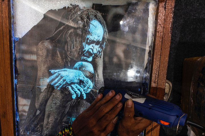 Seorang seniman tengah melukis seorang pemimpin suku Papua di atas kaca. AFP Photo/Juni Kriswanto