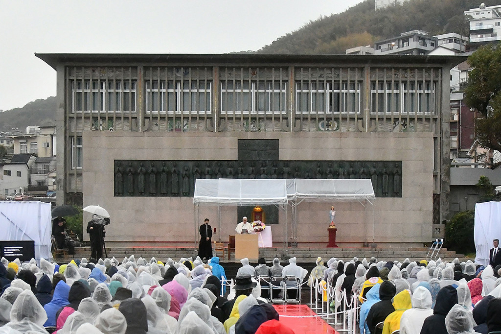 Ratusan orang rela diguyur hujan demi mendengarkan Fransiskus, yang berdiri di samping sebuah foto historis kengerian bom Nagasaki. 