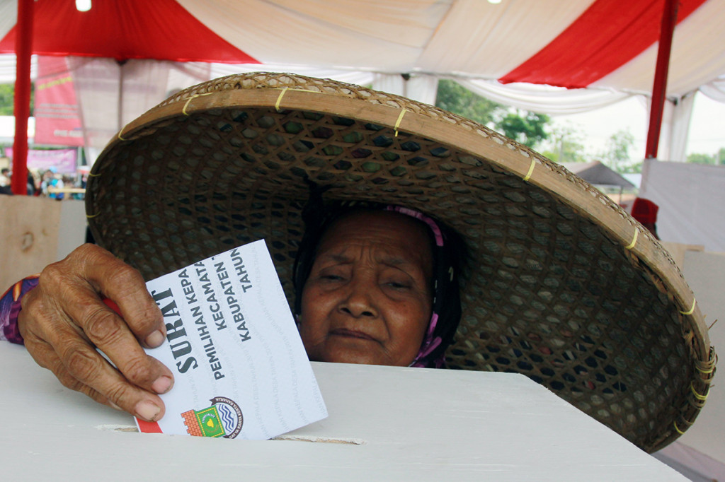 Seorang ibu yang menggunakan topi caping, memasukkan surat suara kedalam kotak saat menggunakan hak pilihnya pada Pemilihan Kepala Desa (Pilkades) serentak Kabupaten Tangerang di Desa Daru, Kabupaten Tangerang.