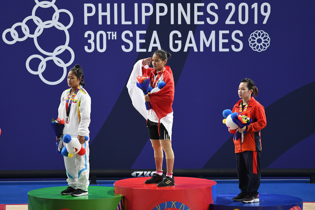 Atlet angkat besi Indonesia Windy Cantika Aisah (tengah) memberi hormat kepada Bendera Merah Putih pada upacara penganugerahan medali pertandingan Angkat Besi 49Kg Wanita SEA Games ke-30 di Stadion RSMC Nino Aquino, Manila, Filipina.