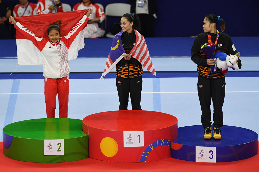 Pesenam Indonesia Irfanaluthfi Rifda (kiri) menbentangkan Bendera Merah Putih pada upacara penganugerahan medali Senam Artistik SEA Games ke-30 di Rizal Coliseum Stadion RSMC Nino Aquino, Manila, Filipina. Peringkat pertama direbut atlet senam Malaysia, Abdul Hadi Farah Ann, dan perunggu juga diraih pesenam Negeri Jiran, Tang Ing Yueh.